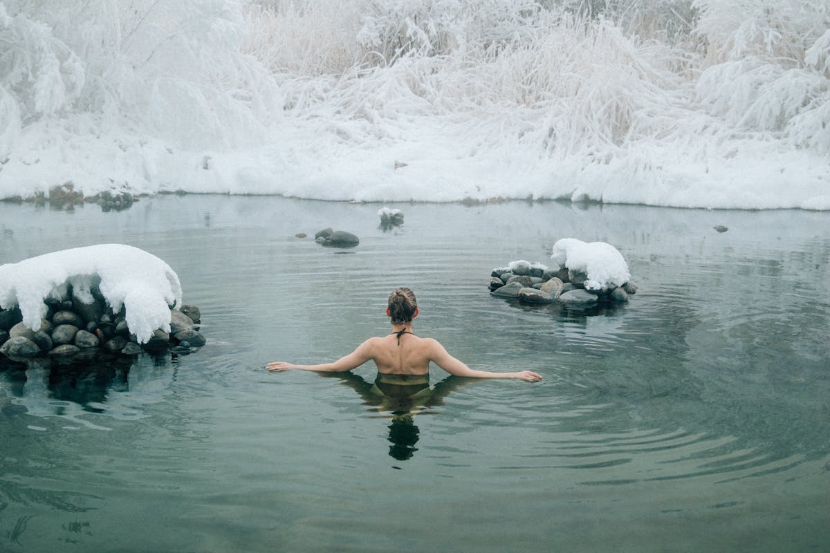A young woman doing Cold Water Therapy in a tranquil winter lake surrounded by snow.