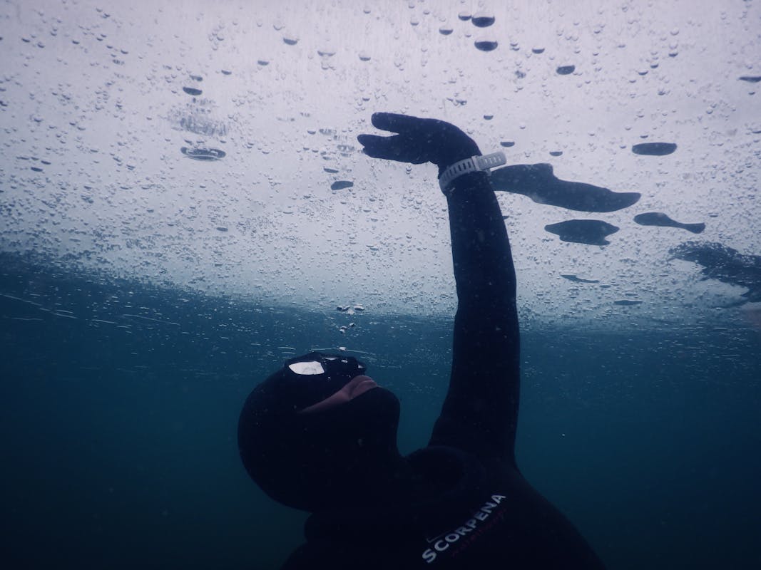 Anonymous diver in mask and wetsuit touching solid ice while swimming under seawater during freediving