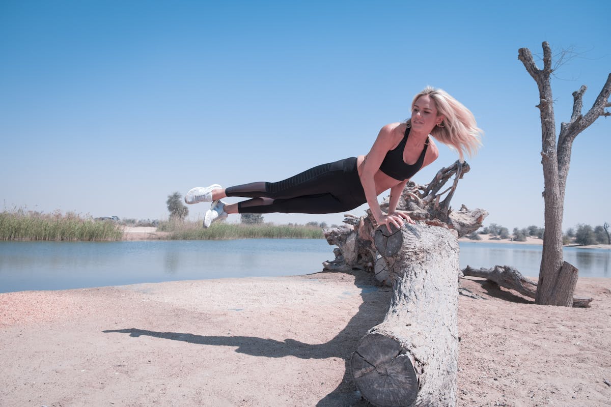 Woman Jump on Tree Log Near Body of Water Under Blue Sky